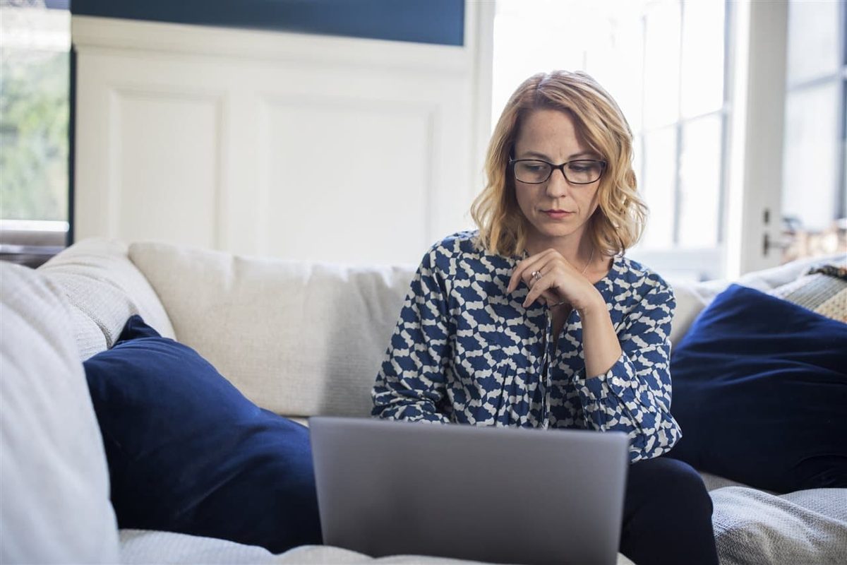 Homeowner sitting on a couch reviewing her laptop carefully to protect her personal information from cybercrime