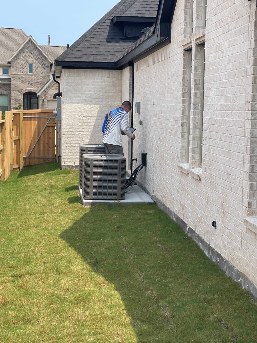 Home inspector evaluating outdoor air conditioning condenser units beside a brick home in the Pearland TX area